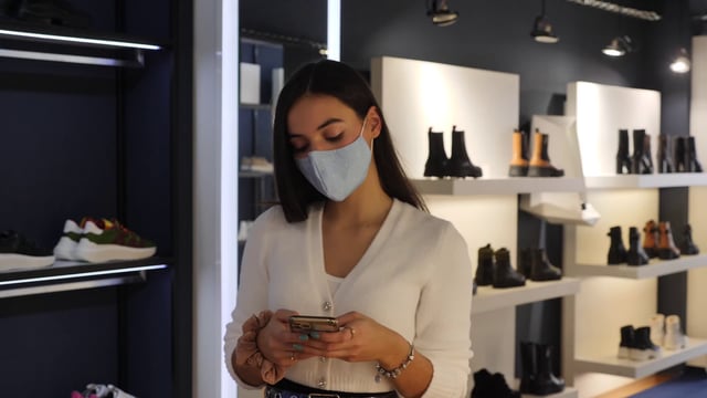 Chica charlando por teléfono inteligente en una tienda de zapatos