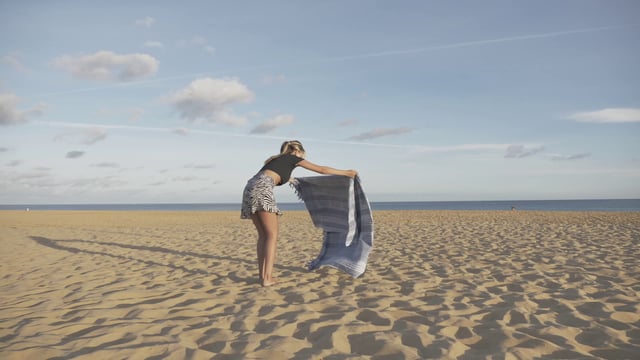 Una niña extiende una toalla en la playa.