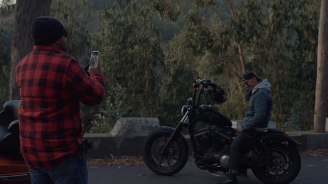 A man taking photos of his friend posing on a motorcycle 