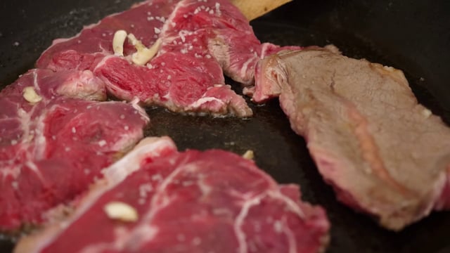 Flipping red meat in a cooking pan