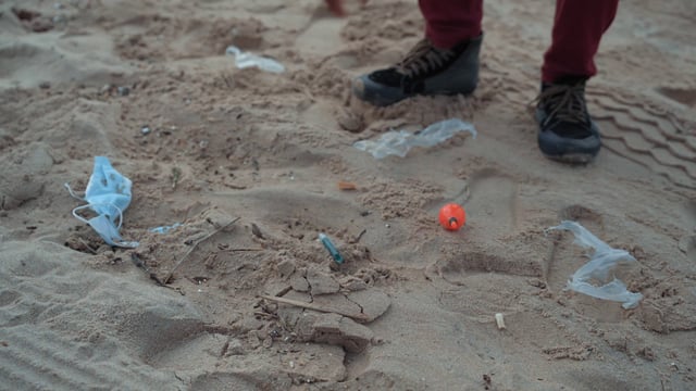 Un chico recoge plástico y otra basura de la arena en la playa.