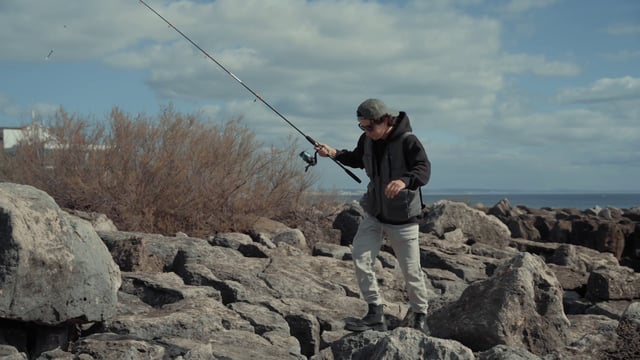 Un pescador va por la orilla rocosa.