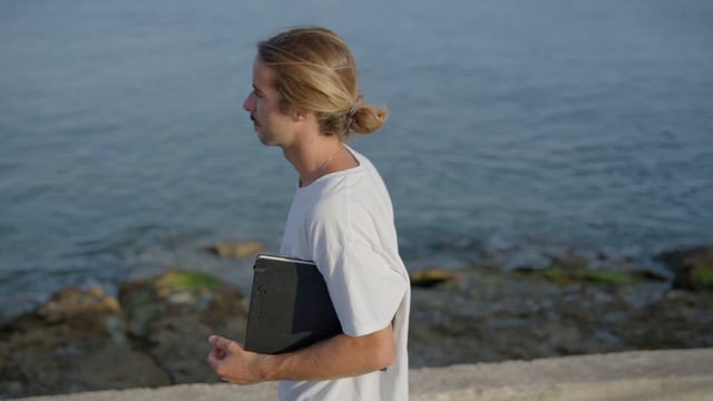 Un artista camina por una costa pedregosa con su cuaderno de bocetos