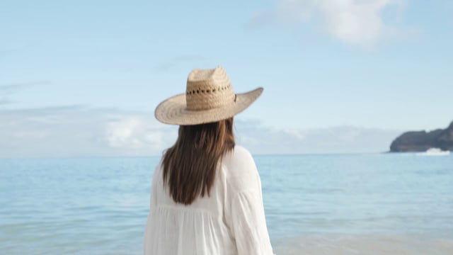戴着帽子的女人沿着海岸散步