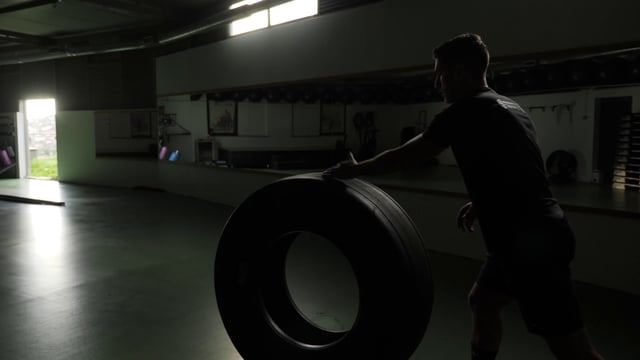 Atleta fuerte rueda el neumático en el gimnasio