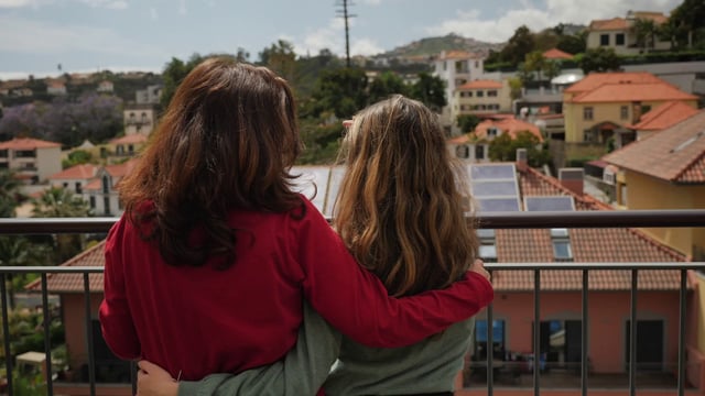 Una madre e hija abrazados de pie en el balcón