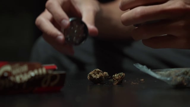 A man putting marijuana buds into a grinder