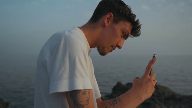 A tattooed guy photographs someone on a beach