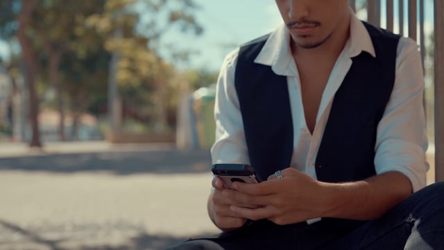 A man typing on his phone while sitting on the curb
