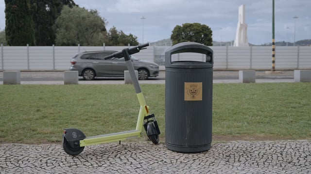 Un scooter eléctrico está estacionado cerca de un cubo de basura.