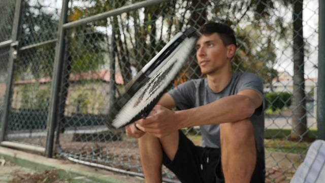 Un tipo gira una raqueta sentado en una cancha de tenis