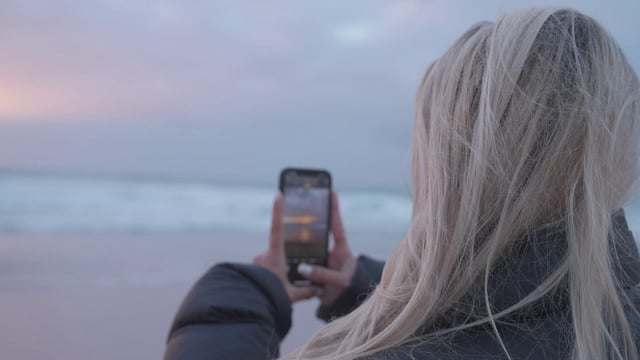 Blonde girl taking photos of the beach at sunset