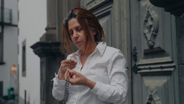 A woman kisses rosary beads near the church