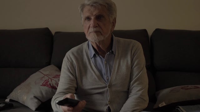 An old man sitting on the couch watching television