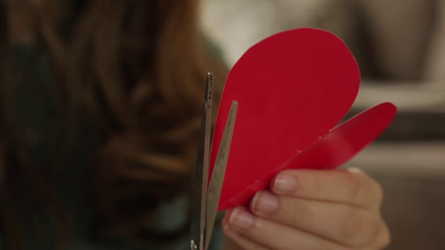 Cerca de una niña corta un corazón rojo de papel con unas tijeras
