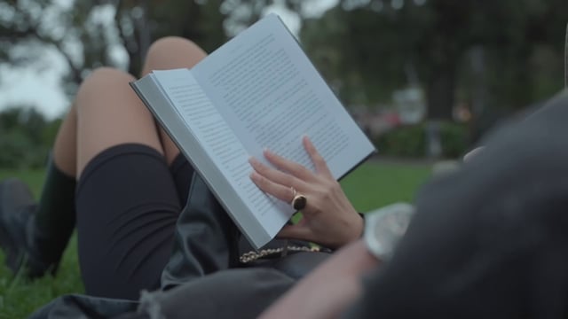 Una niña está leyendo un libro en un parque.