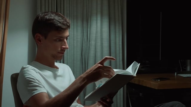 A man carefully reading a book at night