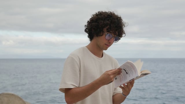 Man reading a book near the ocean