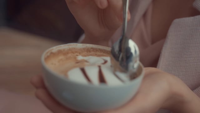 A woman stirring a cappuccino with a teaspoon before tasting it