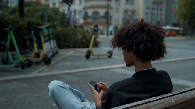 A young man uses his smartphone while sitting on a bench