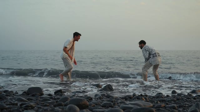 Two young men splash each other with water by the sea