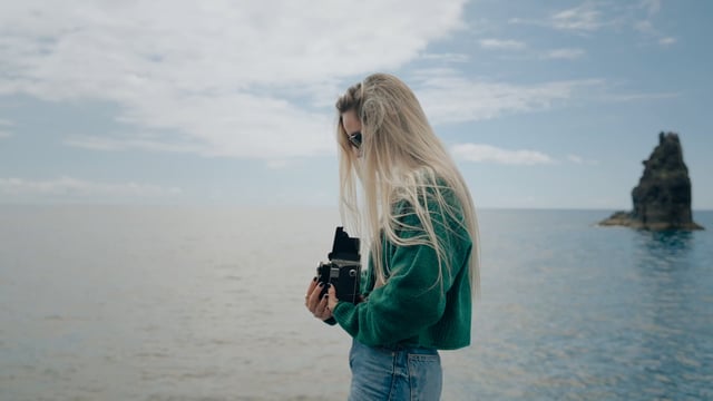 A young woman takes photos of the sea with an old TLR camera