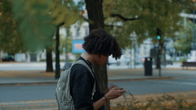 Un chico usa un teléfono inteligente parado en una calle