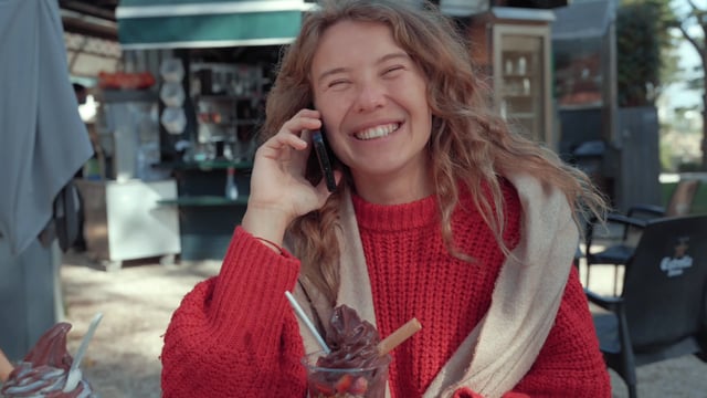 Una niña alegre habla en un teléfono inteligente en un café de la calle