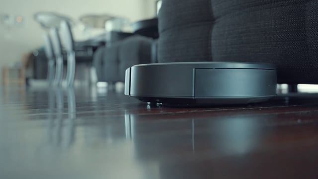 A robot vacuum cleaner cleans the floor near a couch