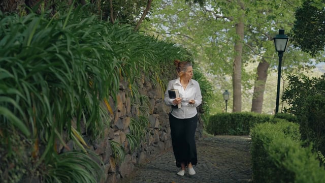 A woman walks in a garden holding a bible