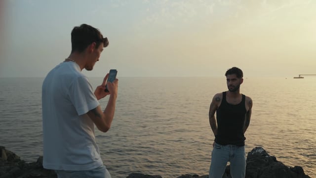 A young man photographs his boyfriend at the beach