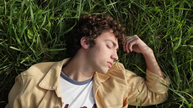 Un chico rizado tumbado en la hierba verde