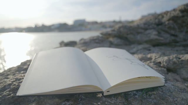 Primer plano de un cuaderno de dibujo en una costa pedregosa