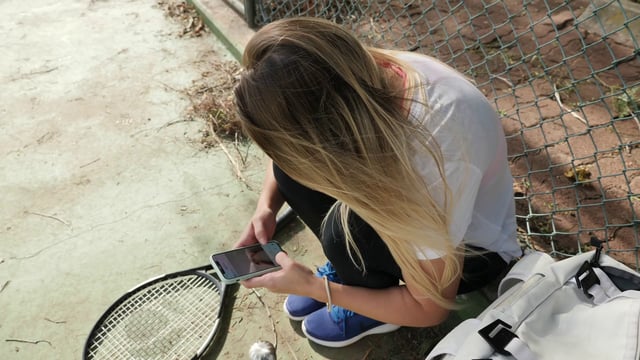 A woman using her phone while sitting on a tennis court