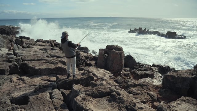 A young man fishing on a rocky beach