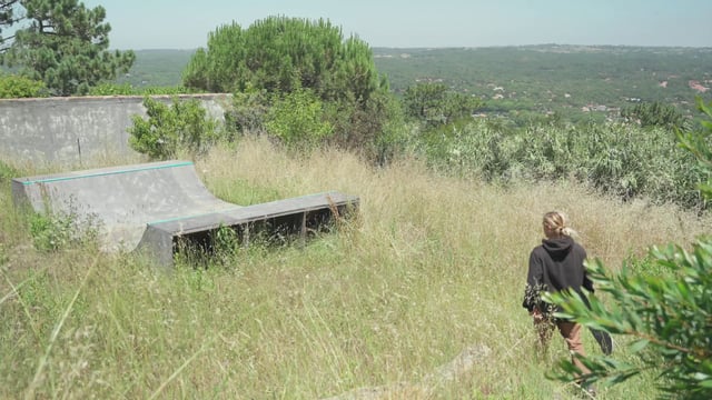 A guy walking to a half-pipe skating ramp in a field