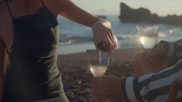 A woman pouring champagne into glasses at sunset on the beach