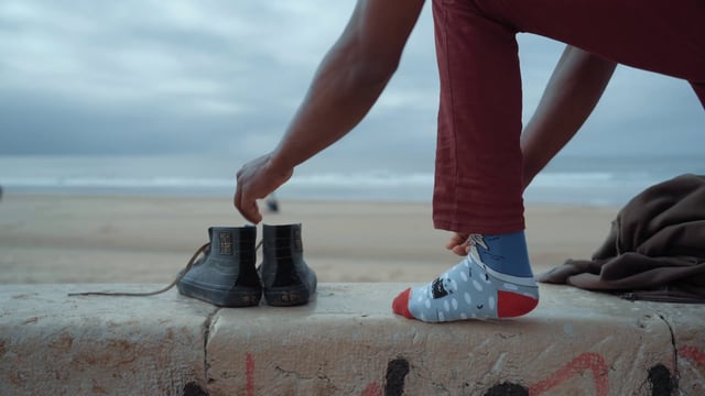 Un chico limpia los zapatos de la arena para ponérselos en las piernas.