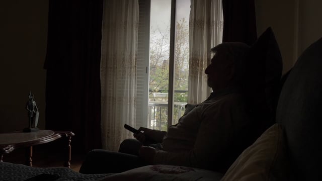 An old man sitting on a couch and changing the TV channel
