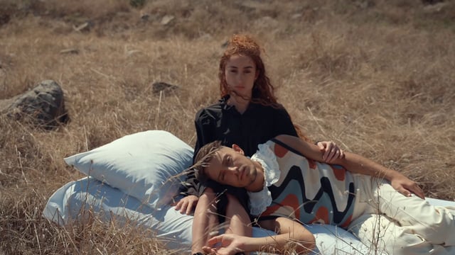 A man and woman are on a bed in the middle of a field