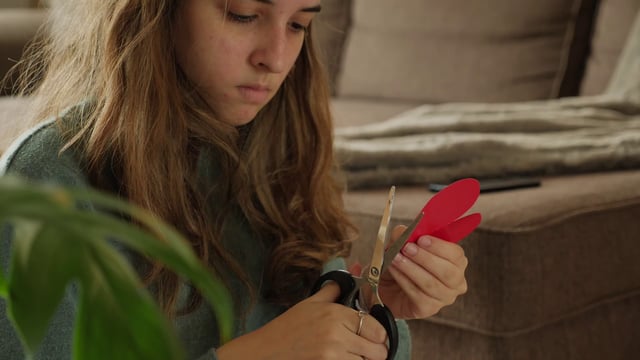 Una niña corta un corazón rojo de papel con unas tijeras