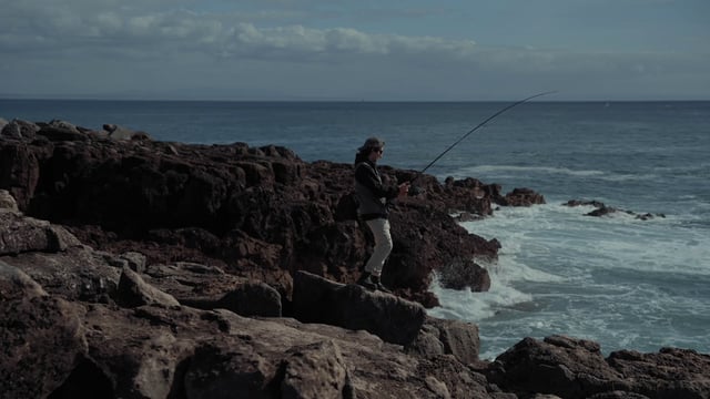 Un joven pescador está pescando en una orilla rocosa.