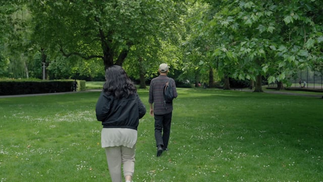 A couple is walking with an Australian shepherd in the park