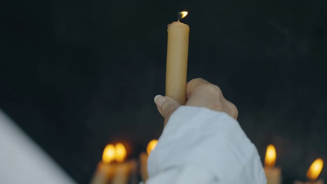 Una mujer pone una vela de la iglesia en el candelero de metal.