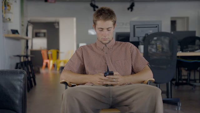 A Man Uses His Smartphone while Sitting on a Chair