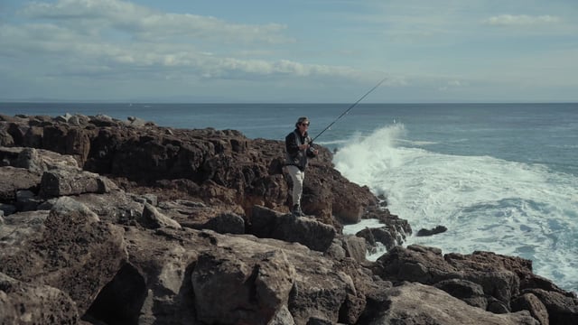Las olas caen sobre las rocas y rocían a un pescador