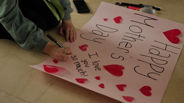 Una hija hace un cartel de saludos para su mamá
