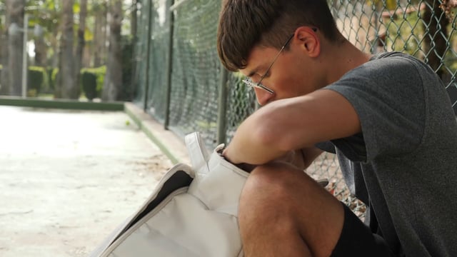 Un chico pone gafas en una mochila después de jugar al tenis