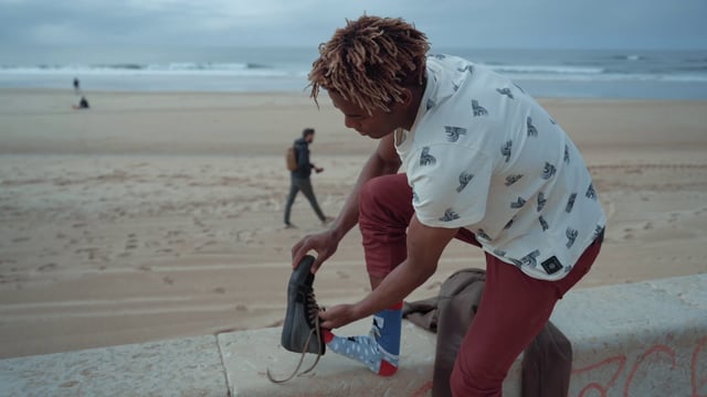Un chico se pone los zapatos en las piernas en la playa.